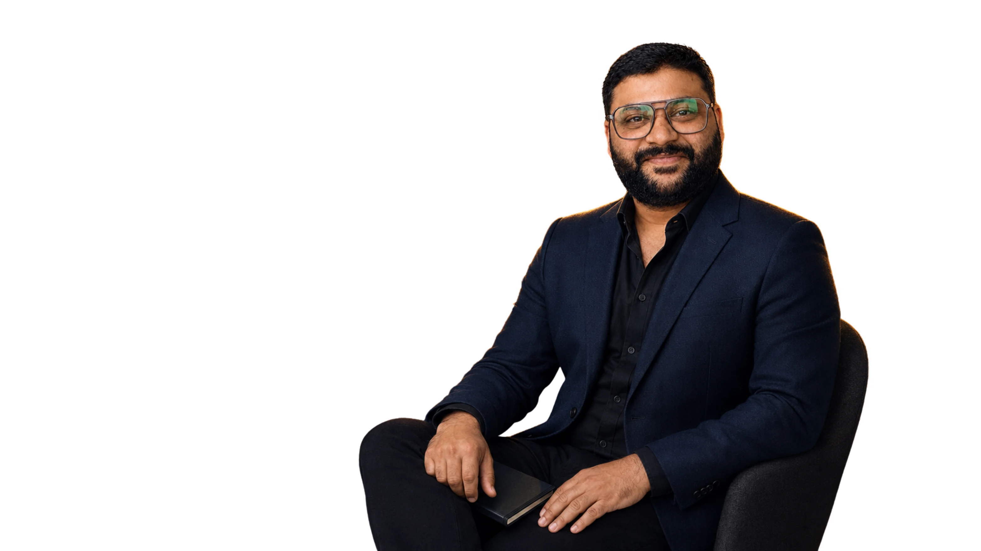 Laxman seated with a notebook in a relaxed executive portrait