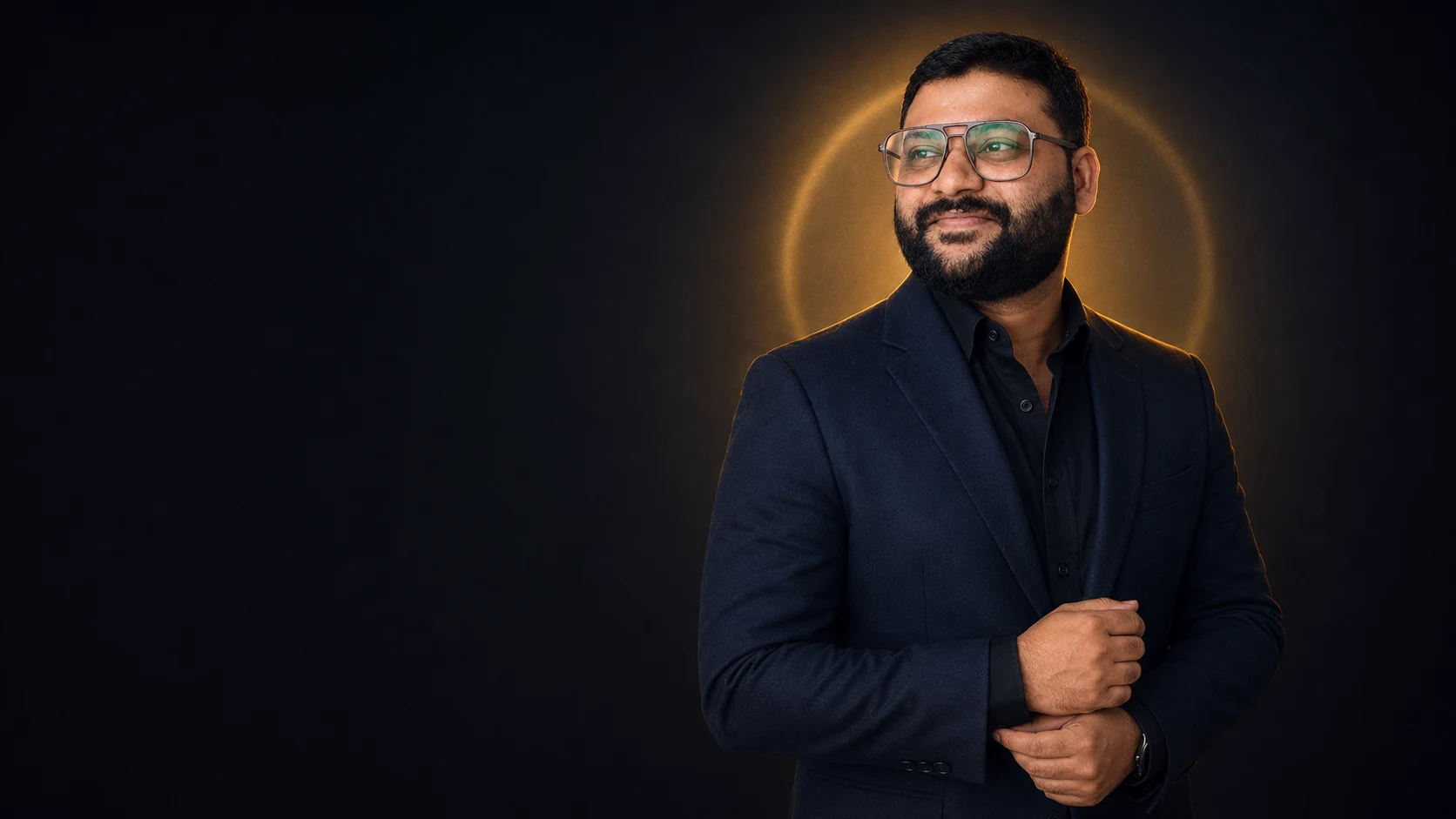 Laxman Pednekar in a navy suit against a dark background with a warm gold halo